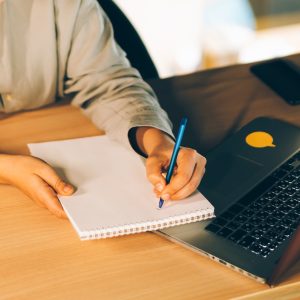 A woman studying online with her laptop, writing in notepad