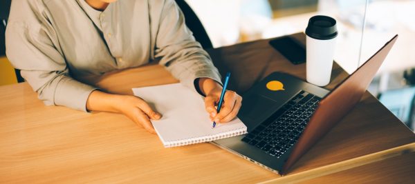 A woman studying online with her laptop, writing in notepad