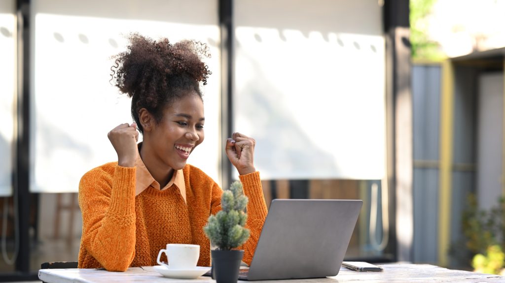 Excited African American woman reading email with good news on laptop.