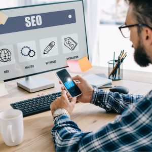 handsome young seo manager using smartphone and computer at workplace